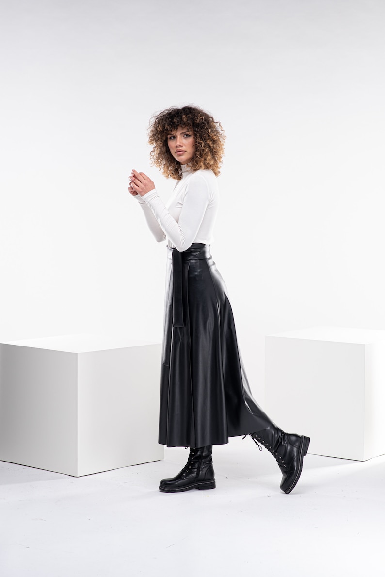 May include: A woman wearing a white turtleneck sweater and a black leather skirt. She is wearing black boots and has curly brown hair.