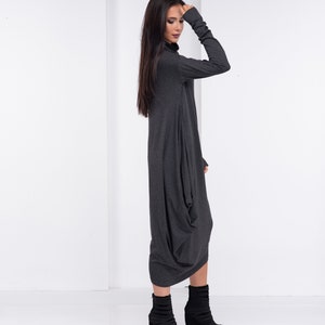 May include: A charcoal gray long-sleeved dress with a loose, flowing fit. The dress has a high neckline and a long, flowing skirt. The model is wearing black ankle boots.