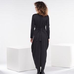 May include: A black long-sleeved dress with a wrap tie at the waist. The dress has a flowing, asymmetrical hemline.