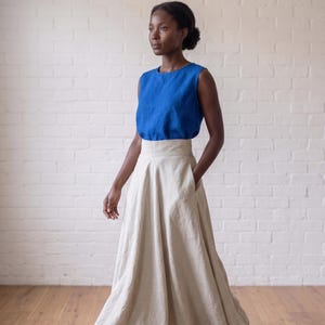 May include: A sleeveless royal blue top with a round neckline paired with a high-waisted, floor-length beige skirt. The skirt features a wide waistband, a full, flowing silhouette, and side pockets, creating a two-piece ensemble with a clean look.