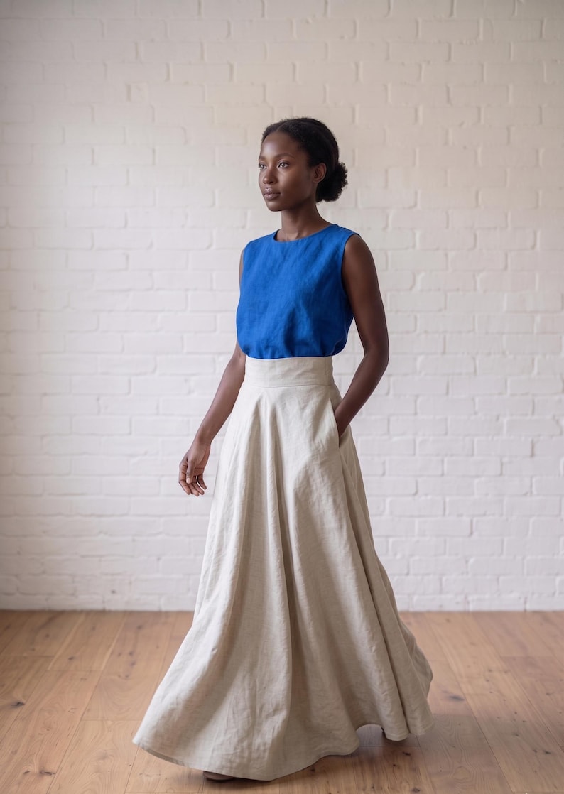 May include: A sleeveless royal blue top with a round neckline paired with a high-waisted, floor-length beige skirt. The skirt features a wide waistband, a full, flowing silhouette, and side pockets, creating a two-piece ensemble with a clean look.