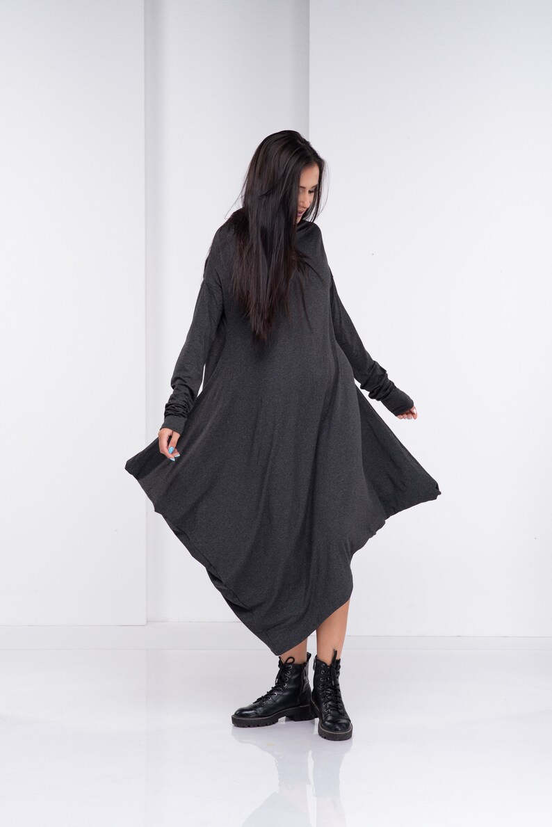 May include: A long, charcoal gray, asymmetrical dress with long sleeves and a cowl neck. The dress is made of a soft, stretchy fabric and has a relaxed fit. The model is wearing black ankle boots.