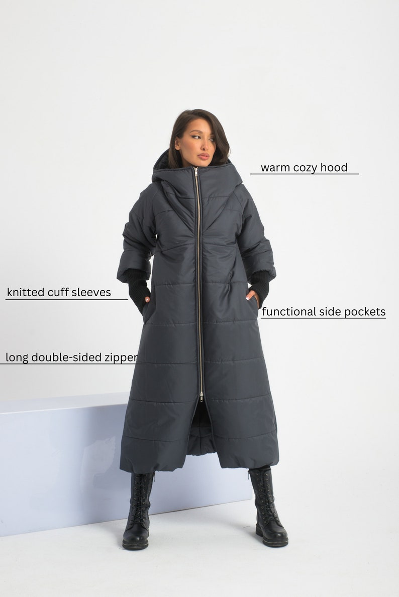 May include: A long, dark grey puffer coat with a warm cosy hood, knitted cuff sleeves, and a long double-sided zipper. The coat has functional side pockets.