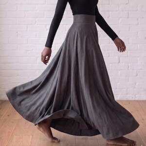 May include: A long, charcoal grey maxi skirt with a high-waisted, fitted waistband and a full, flowing silhouette that flares out towards the hem. The skirt is paired with a long-sleeved black top that features a simple, fitted design.