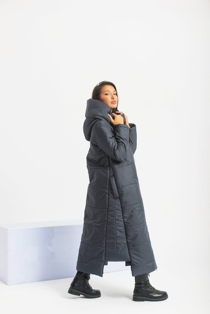 Long hooded puffer jacket with asymmetrical design in quilted 150g fabric, featuring a double front zipper, side pockets, and viscose lining. Edgy, cyberpunk-inspired style for a bold, modern winter look.