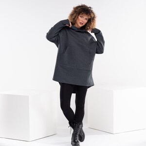 May include: A gray oversized hoodie with a kangaroo pocket and a drawstring hood. The model is wearing black leggings and black combat boots.