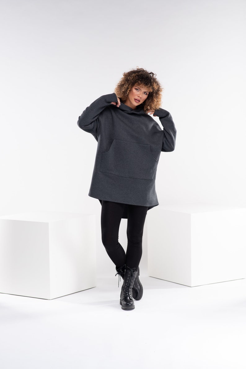 May include: A gray oversized hoodie with a kangaroo pocket and a drawstring hood. The model is wearing black leggings and black combat boots.