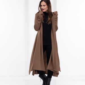 May include: A long brown cardigan with a hood and long sleeves. The cardigan is open in the front and has a flowing design. The model is wearing black pants and black boots.