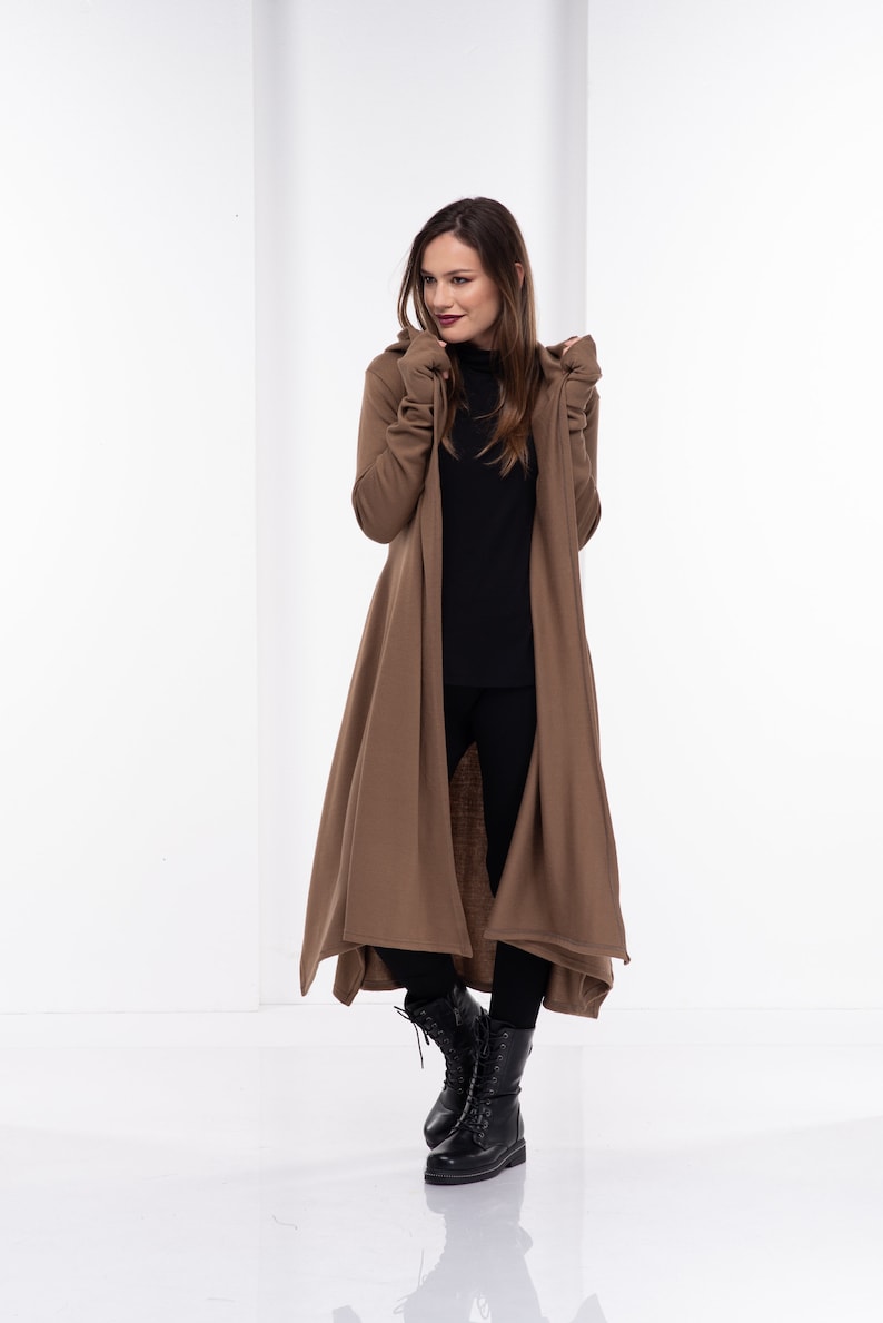 May include: A long brown cardigan with a hood and long sleeves. The cardigan is open in the front and has a flowing design. The model is wearing black pants and black boots.