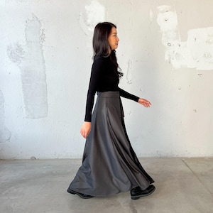 May include: A woman wearing a black long-sleeved turtleneck shirt and a long, flowing gray skirt with a black belt. She is walking towards the right side of the image.