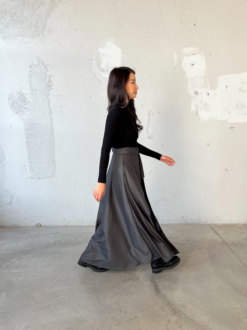 May include: A woman wearing a black long-sleeved turtleneck shirt and a long, flowing gray skirt with a black belt. She is walking towards the right side of the image.