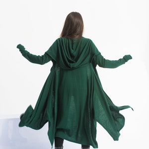 May include: A long, dark green hooded cardigan with a flowing, asymmetrical hem. The cardigan is made of a soft, knit fabric and has a relaxed fit.