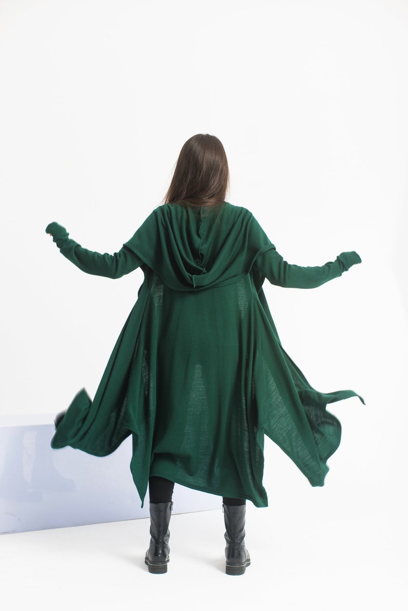May include: A long, dark green hooded cardigan with a flowing, asymmetrical hem. The cardigan is made of a soft, knit fabric and has a relaxed fit.