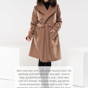 May include: A brown hooded wrap coat with a tie belt. The coat has two pockets and is shown on a model. The text "Best coat ever: arm, soft, great neutral color, fits perfectly and stitched very, very well. I love it! Olga out did herself on this coat. I shall take care of it forever. Nice arm length, wonderful hood and pockets set just right to use. I am extremely pleased, will trust this seller for more garment. Arrived 5 days earlier than expected." is below the model.