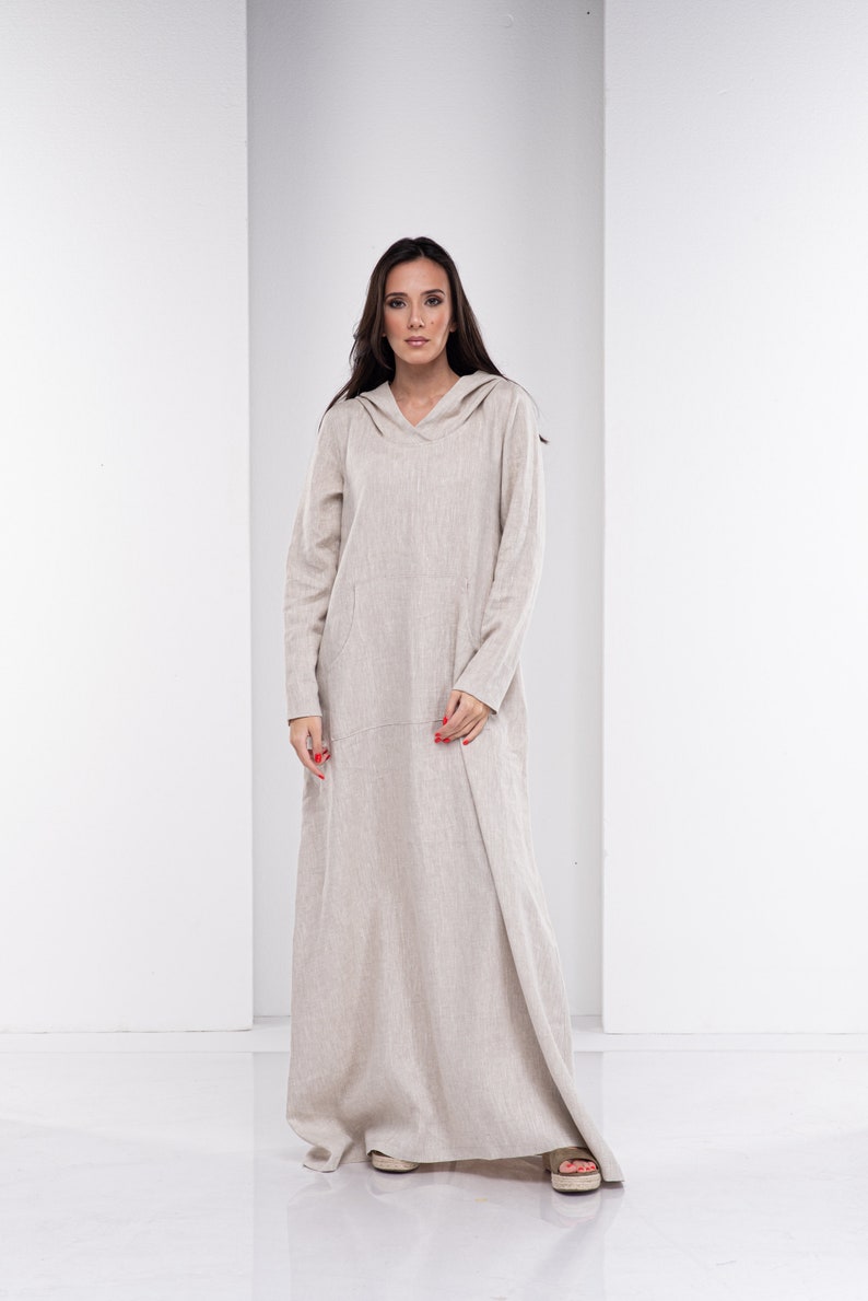 May include: A long, beige linen dress with a hood and a V-neck. The dress has a relaxed fit and a flowing silhouette.