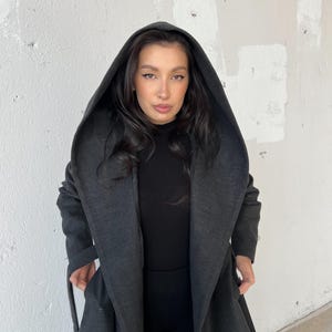 Puede incluir: Una larga gabardina gris oscuro con capucha, cuello ancho y cintur&oacute;n de anudar. La gabardina est&aacute; hecha de una tela suave y c&oacute;moda y tiene un corte holgado.