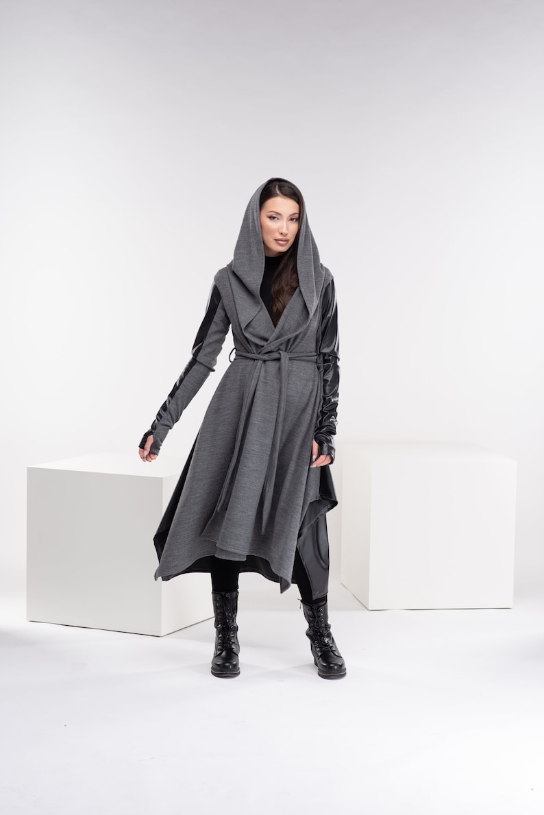 May include: A gray hooded wrap coat with black leather sleeves and a black belt. The coat has a long, flowing silhouette and a relaxed fit.