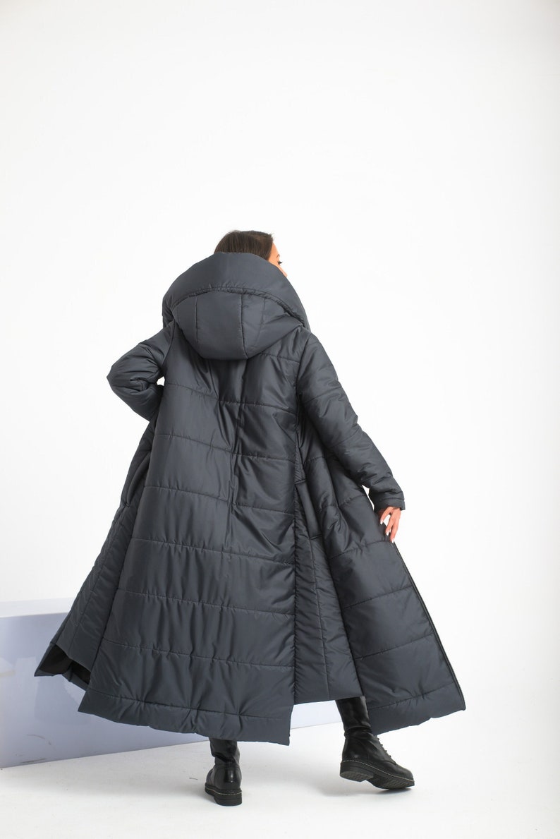 May include: A long, dark blue puffer coat with a large hood. The coat has a quilted design and a slightly flared silhouette.