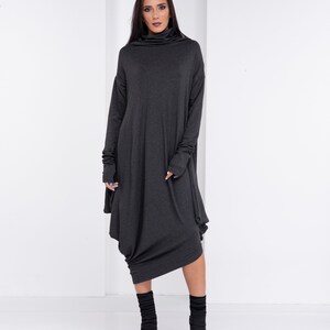 May include: A charcoal gray long-sleeved dress with a cowl neck and a loose, flowing fit. The dress has a unique asymmetrical hemline and is styled with black ankle boots.