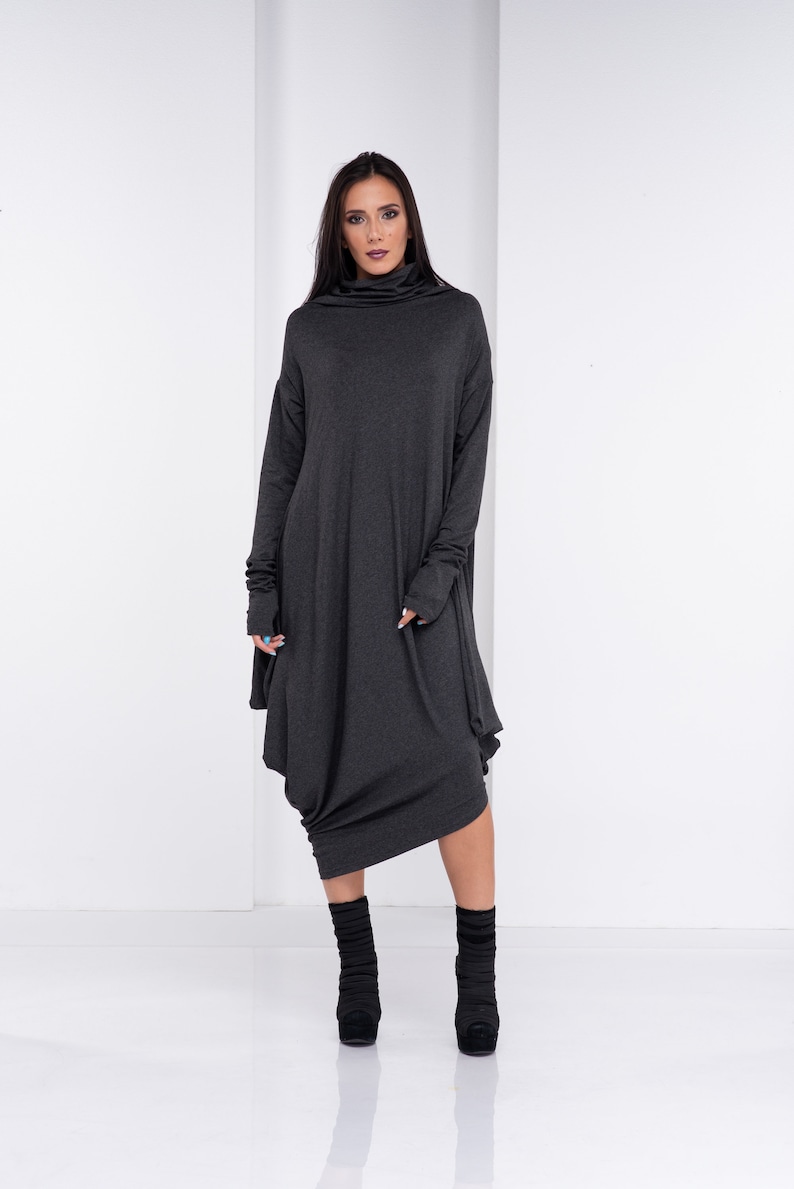 May include: A charcoal gray long-sleeved dress with a cowl neck and a loose, flowing fit. The dress has a unique asymmetrical hemline and is styled with black ankle boots.
