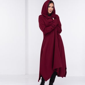 May include: A woman wearing a long, burgundy hooded cardigan with a draped asymmetrical hem. She is standing on a white background.