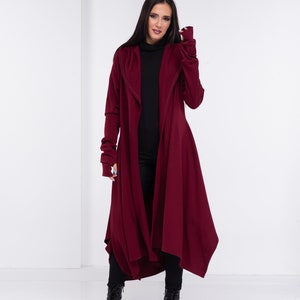 May include: A long, burgundy cardigan with a hood and long sleeves. The cardigan is open in the front and has a flowing, asymmetrical hemline.