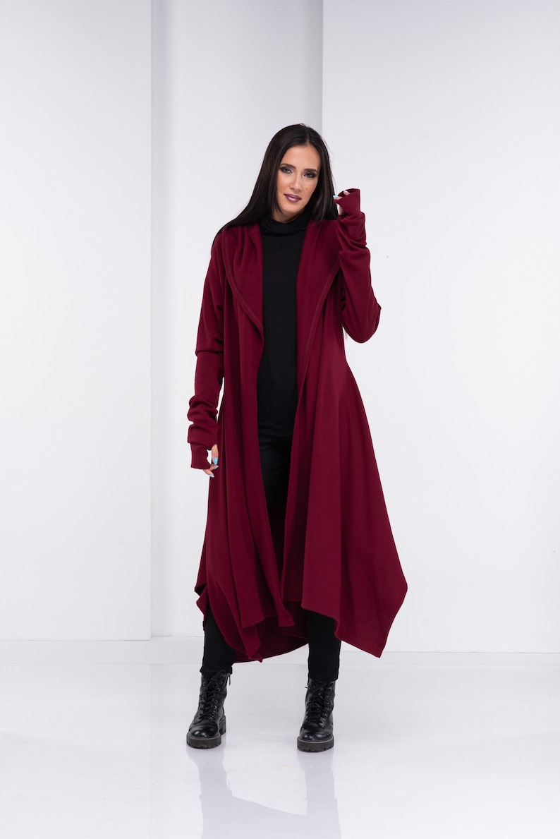 May include: A long, burgundy cardigan with a hood and long sleeves. The cardigan is open in the front and has a flowing, asymmetrical hemline.