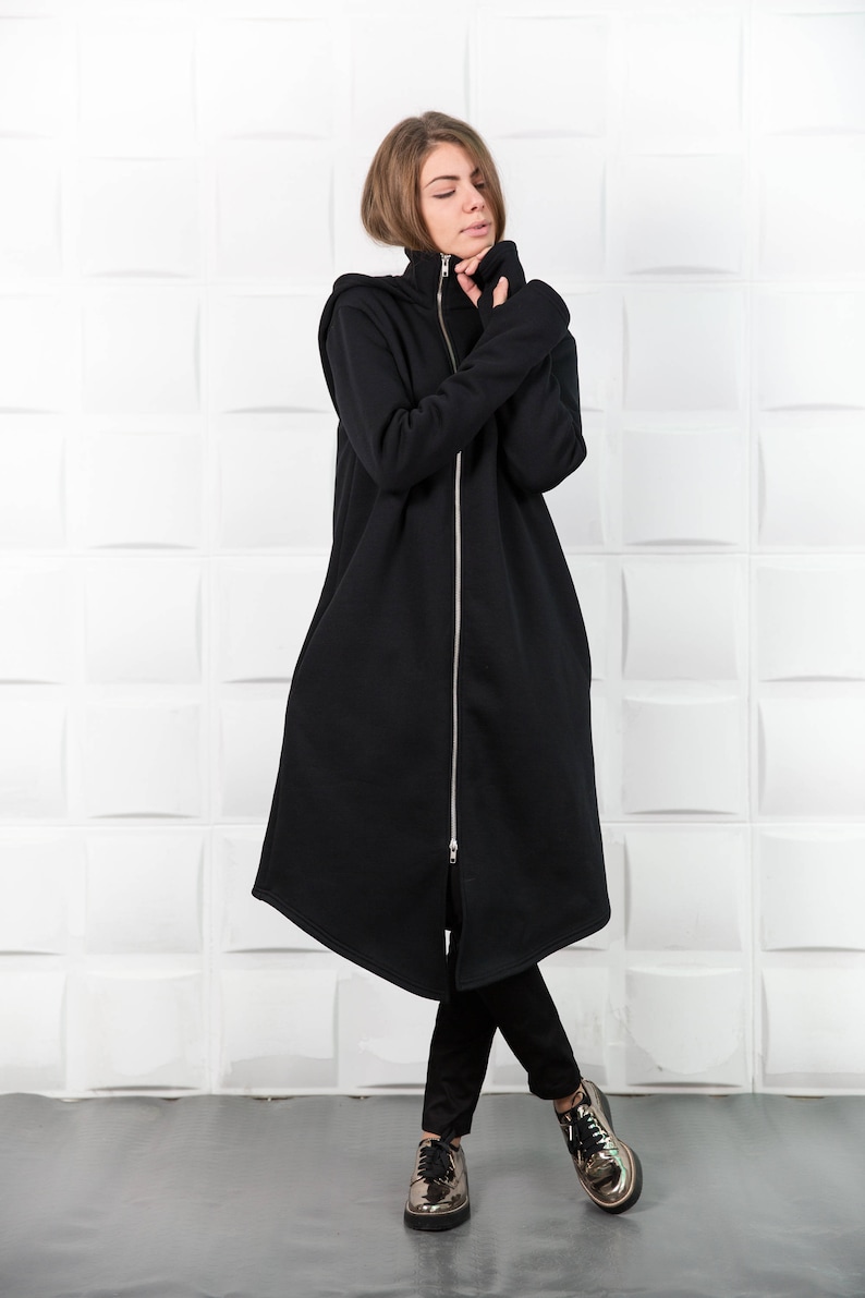 May include: A long black hooded sweatshirt with a zipper down the front. The sweatshirt has a high neck and long sleeves. The model is wearing black pants and gold shoes.