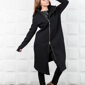 May include: A long black hooded sweatshirt with a zipper down the front. The sweatshirt has a long, asymmetrical hemline and thumbholes at the cuffs.