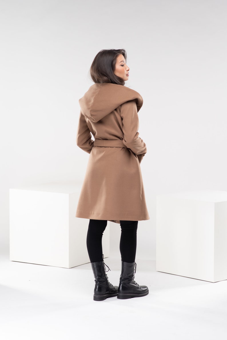 May include: A brown hooded coat with a belt, worn by a person with long dark hair. The coat is belted at the waist and has a large hood.