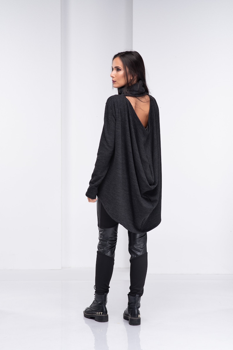 May include: A charcoal gray long-sleeved shirt with a cowl neck and a large open back detail. The shirt is worn with black leggings and black boots.