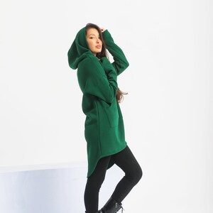 May include: A woman wearing a long, dark green hooded sweatshirt with a high-low hemline and black leggings. She is wearing black lace-up boots.