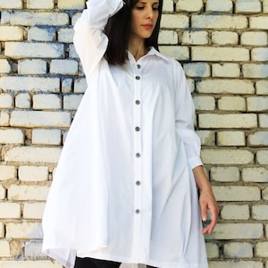 May include: A white oversized button-down shirt with long sleeves and a relaxed fit. The shirt is made of a lightweight fabric and has a slightly A-line silhouette.