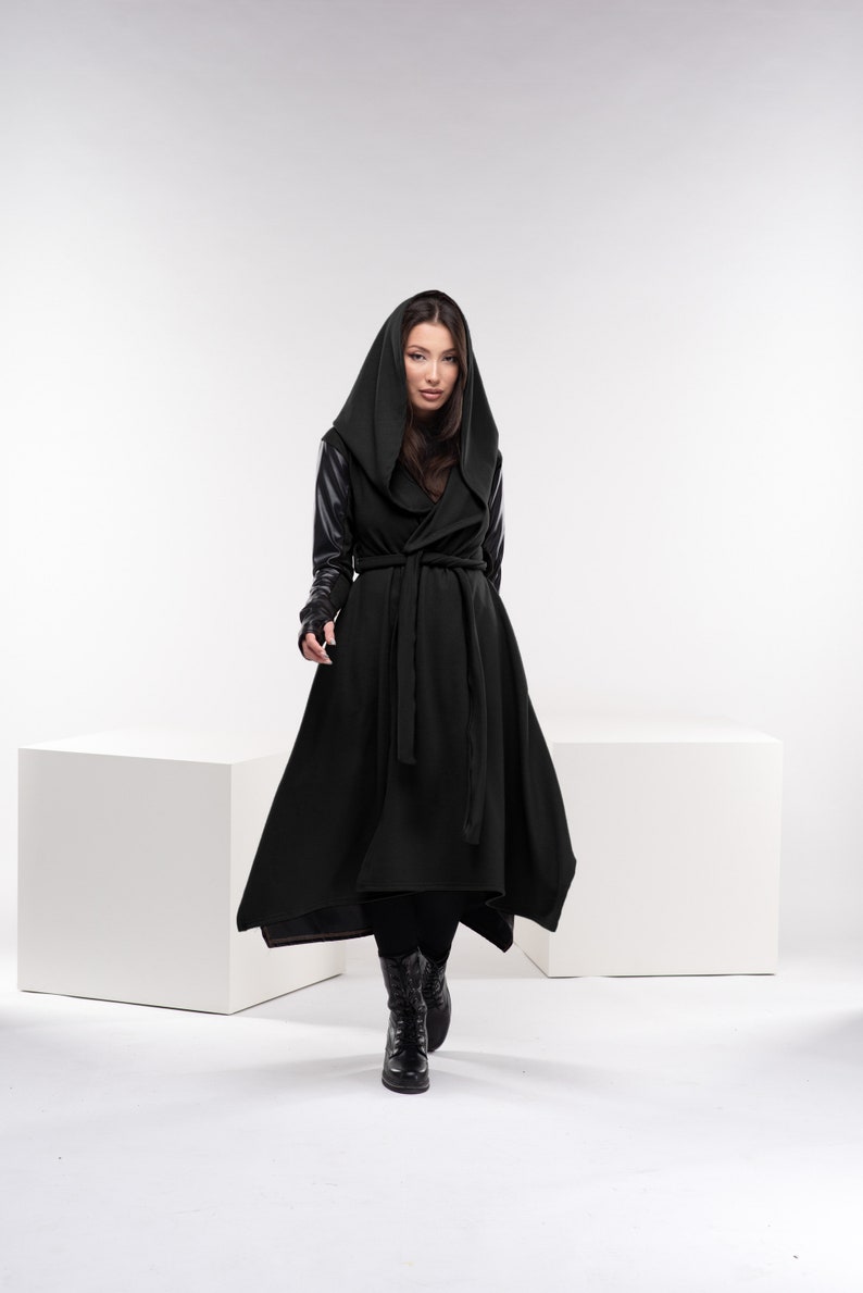 May include: A black hooded coat with a long, flowing skirt and leather sleeves. The coat is belted at the waist and has a relaxed fit.