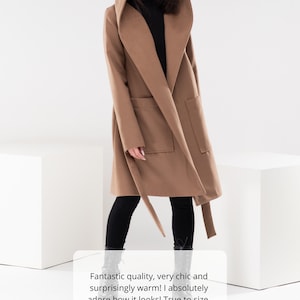 May include: A brown hooded wrap coat with a tie belt and large pockets. The coat is worn by a person standing on a white surface. The text "Fantastic quality, very chic and surprisingly warm! I absolutely adore how it looks! True to size, and love the big pockets!" is displayed below the image. Five yellow stars are displayed below the text.