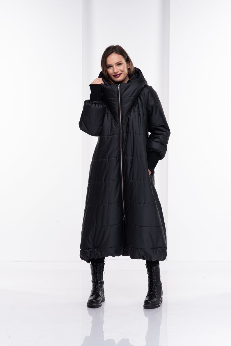 May include: A long black puffer coat with a high collar and a zip fastening. The coat has a quilted design and a slightly flared shape.