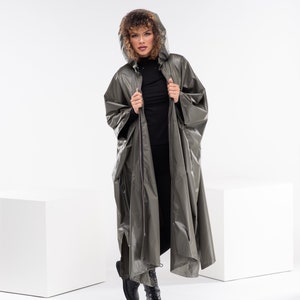May include: A long, olive green hooded raincoat with a zipper closure. The raincoat has a relaxed fit and is made of a water-resistant material.