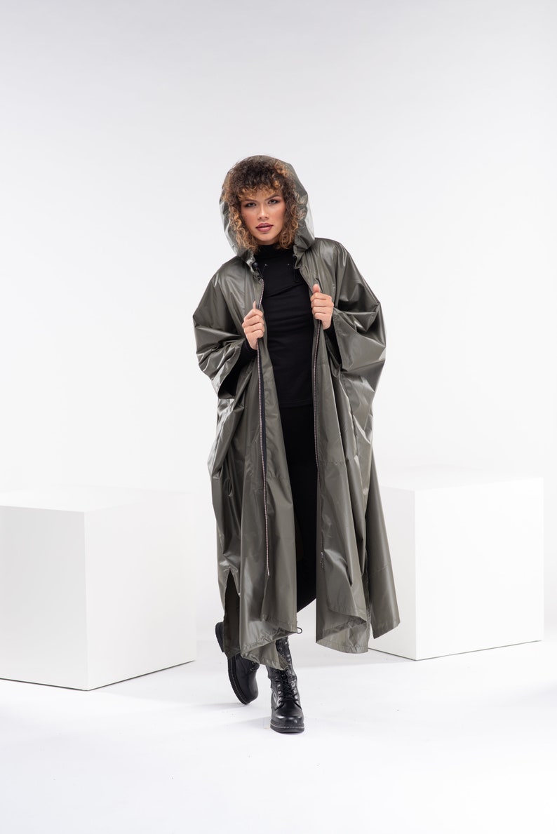 May include: A long, olive green hooded raincoat with a zipper closure. The raincoat has a relaxed fit and is made of a water-resistant material.