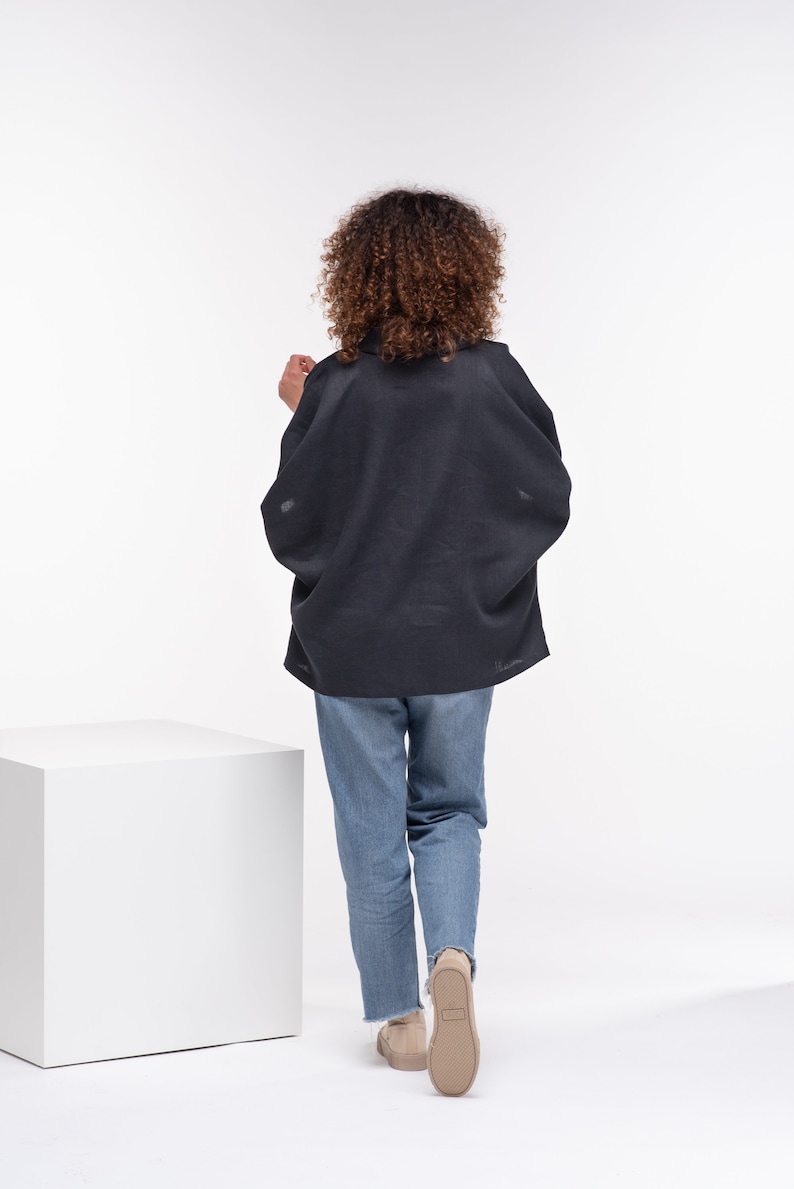 Puede incluir: Una persona lleva una blusa de lino gris oscuro de corte holgado y pantalones vaqueros azules. Se aleja de la c&aacute;mara, de espaldas al espectador.