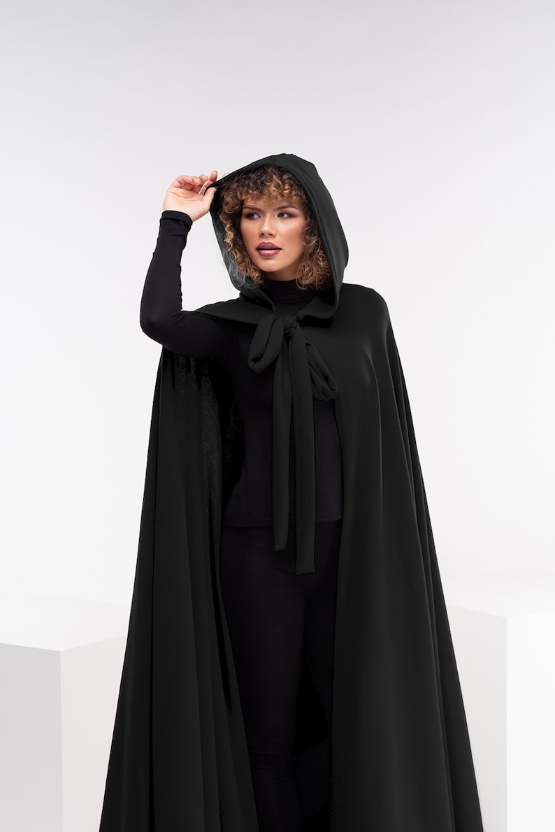 May include: A black hooded cape with a tie closure. The cape is made of a soft, flowing fabric.
