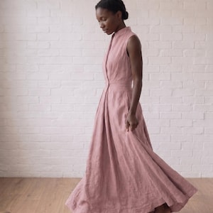 May include: A sleeveless, floor-length dress in a dusty rose color. The garment features a high collar, a button-down front closure, and a fitted bodice that transitions into a full, flowing skirt with visible pleats at the waistline.