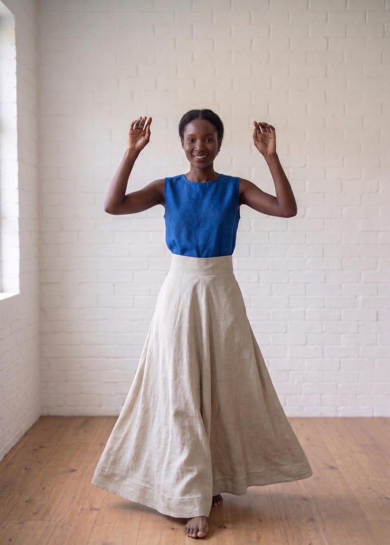 May include: A sleeveless royal blue top with a high neckline paired with a floor-length, high-waisted beige skirt. The skirt features a wide waistband and a full, flowing silhouette that reaches the floor, creating a simple two-piece ensemble.