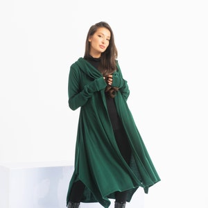 May include: A long, dark green hooded cardigan with long sleeves and a flowing hemline. The cardigan is worn by a person with long dark hair and is paired with black pants and black boots.