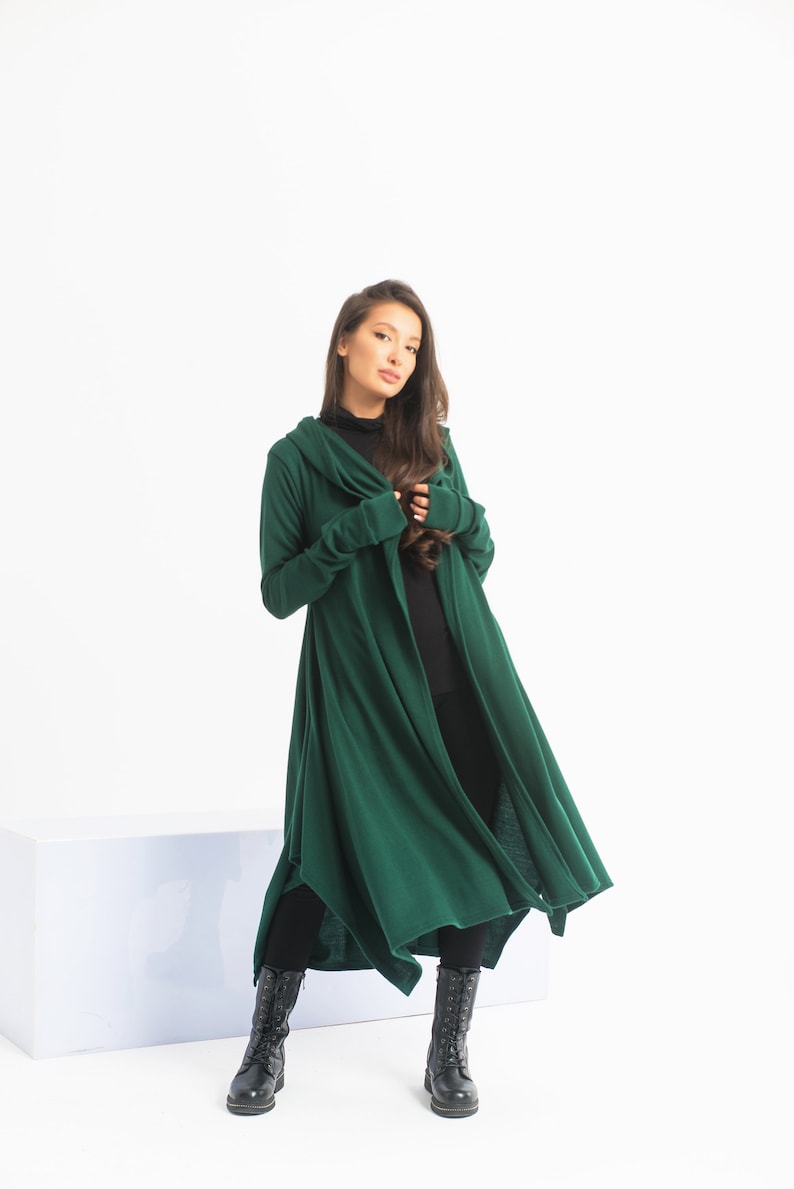 May include: A long, dark green hooded cardigan with long sleeves and a flowing hemline. The cardigan is worn by a person with long dark hair and is paired with black pants and black boots.