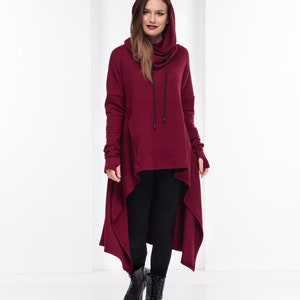 May include: A long, burgundy hooded sweatshirt with a high neckline and a long, asymmetrical hem. The sweatshirt has a drawstring hood and long sleeves.