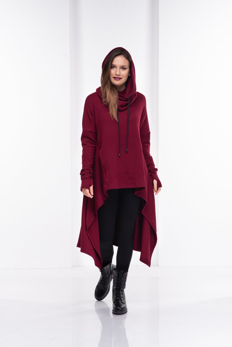 May include: A long, burgundy hooded sweatshirt with a high neckline and a long, asymmetrical hem. The sweatshirt has a drawstring hood and long sleeves.