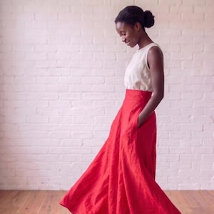 May include: A sleeveless white top paired with a high-waisted, floor-length red skirt. The skirt features a wide, flowing silhouette with a full hemline and side pockets, creating a distinct contrast between the neutral bodice and the vibrant skirt.
