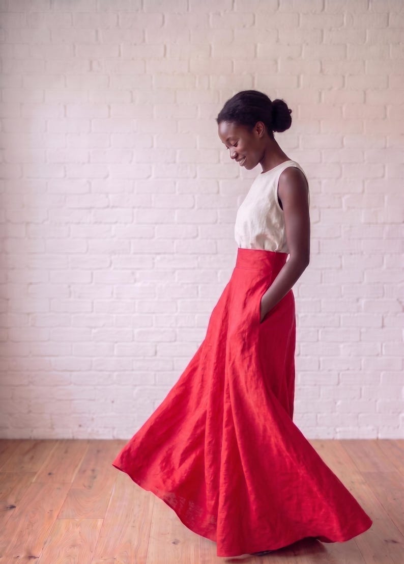 May include: A sleeveless white top paired with a high-waisted, floor-length red skirt. The skirt features a wide, flowing silhouette with a full hemline and side pockets, creating a distinct contrast between the neutral bodice and the vibrant skirt.