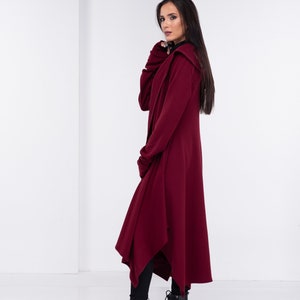 May include: A long, burgundy hooded cardigan with a draped asymmetrical hem. The cardigan is made of a soft, comfortable fabric and has a relaxed fit.