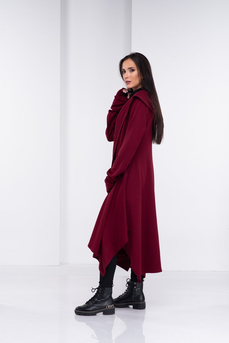 May include: A long, burgundy hooded cardigan with a draped asymmetrical hem. The cardigan is made of a soft, comfortable fabric and has a relaxed fit.